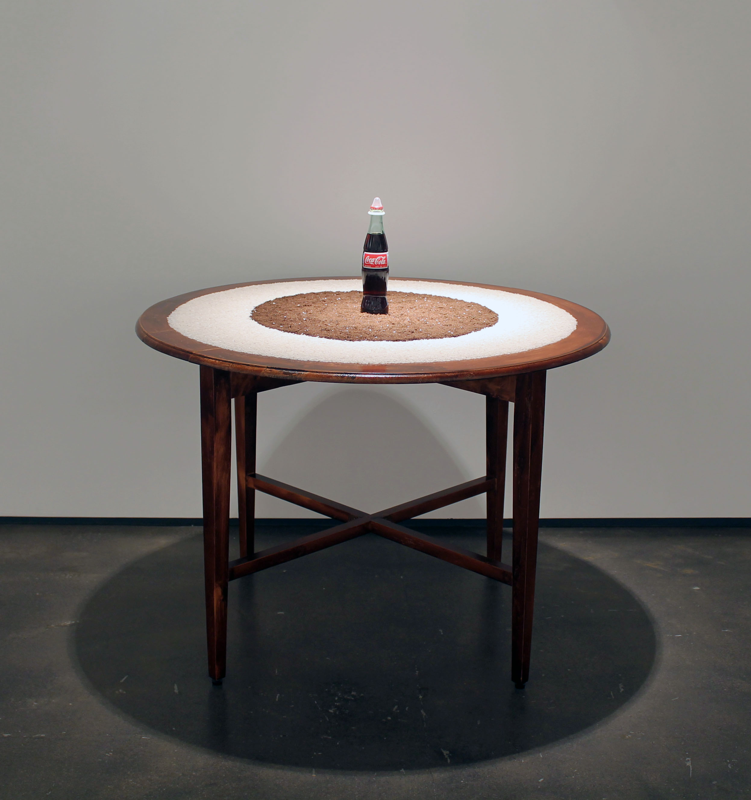 <center><em>Sacred Coke</em>, 1994-2014, wooden table, organic rice, soil, Coca-Cola bottle, and condom,  40 ½ x 41 x 41 in. (102.5 x 457 x 71 cm)</center>